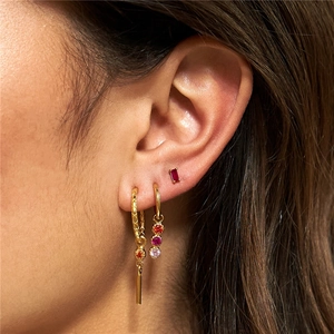 Close-up of golden earring set with red and pink gemstones worn on model's ear