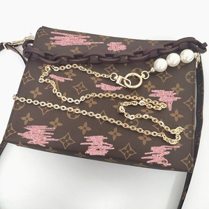 Detail of monogram toiletry bag with gold chain, brown link strap and pearl charms