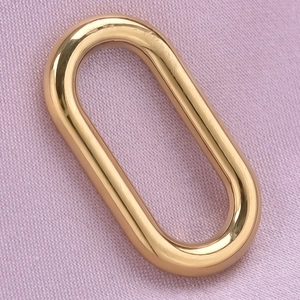Macro view of a polished golden oval stainless steel pendant on soft purple fabric