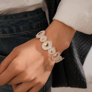 Gros plan d'un bracelet bohème doré avec émail crème porté sur le poignet