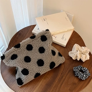 Close-up of fuzzy polka dot makeup bag on a wooden table with lifestyle props
