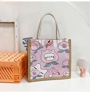 Detail of pink canvas tote bag with cute cartoon peach and cat prints and woven rope handles