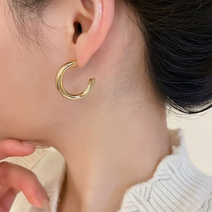 Close-up of chunky gold C-shaped hoop earrings with polished mirror finish on model