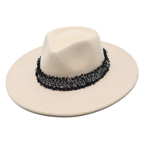 Détail d'un chapeau fedora beige avec un ruban en tweed noir et blanc chic et des franges