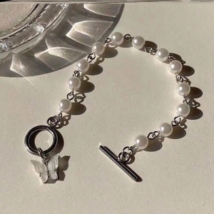 Detailed view of silver cross necklace with pearls, butterfly charm and T-bar toggle clasp