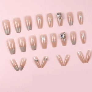 Coffin-shaped cream and glitter press-on nails with rhinestone accents on pink background