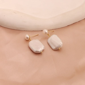 Detailed macro shot of baroque drop earrings with dual pearls on silk fabric