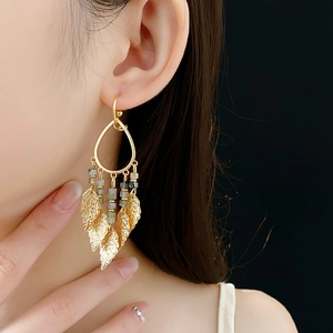 Gros plan de boucles d'oreilles dorées avec feuilles et pompons sur un modèle