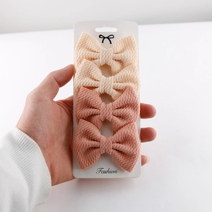 Detail of four fabric bow hair clips in beige and dusty pink on a fashion display card