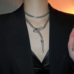 Close-up of silver snake necklace with green gems and tassel on a female model