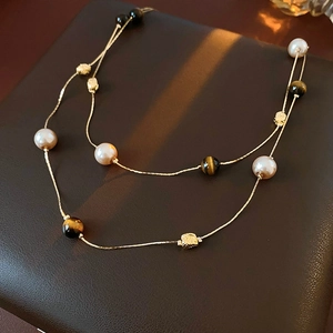 Detail of layered gold necklace with white pearls and tiger eye stone on leather