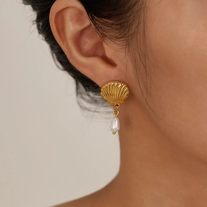 Detail of gold seashell earrings with white teardrop pearl on a model for French vintage style