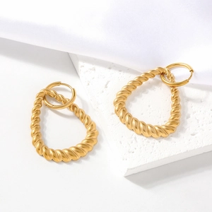 Elegante goldene gedrehte Tropfenohrringe auf einem weißen Steinhintergrund
