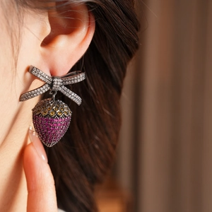 Macro view of vintage strawberry bow earrings featuring pink zircon on dark metal