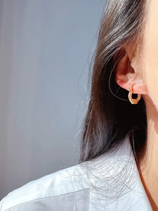 Close-up of golden U-shaped earrings with textured patterns on a model's ear