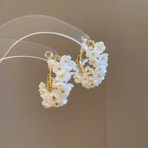 Detailed close-up of C-shaped floral earrings with white petals and golden metal wire