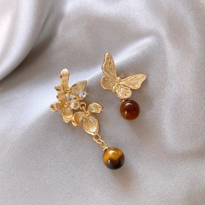 Detail view of asymmetrical flower and butterfly gold earrings with brown tiger eye beads