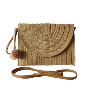 Khaki straw clutch bag with brown PU strap and pompom tassel on white background