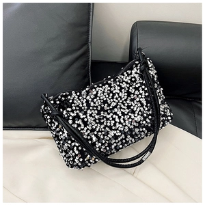 Detail of sequined baguette bag with silver accents and leather strap on a sofa