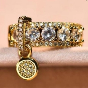 Minimalist gold ring with circular zircon disc pendant on pink velvet background