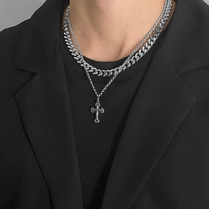 Close-up of double-layer silver cross necklace and Cuban link chain on a black suit