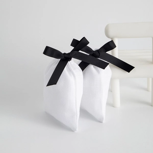 Detailed view of white drawstring jewelry pouches with elegant black ribbon bows