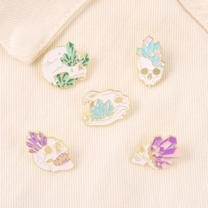 Set of five skull and crystal enamel pins displayed on a soft white knit texture background