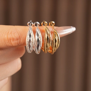 Close-up of C-shaped hoop earrings in gold and silver with matte and polished textures