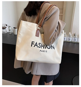 Detail view of large canvas tote bag with leather straps and Fashion Paris text on model