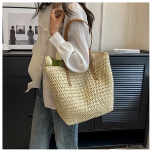 Detail of hollow woven tote bag with brown leather shoulder strap and white stitching