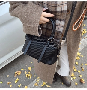 Makro-Detail der schwarzen Plissee-Handtasche mit goldener Hardware und Rundgriff