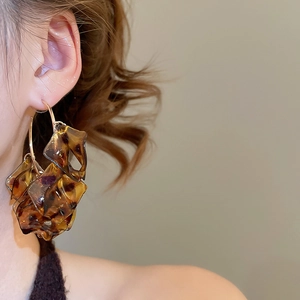 Macro shot of gold C-shaped earrings with leopard resin petals worn by a model