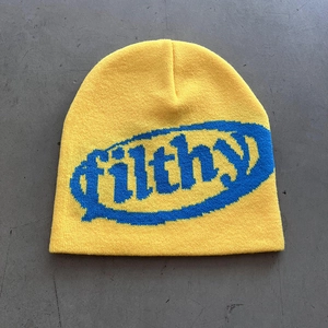 Detailed top view of a yellow knitted beanie featuring blue jacquard filthy lettering