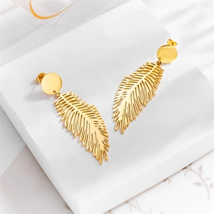 Minimalist gold feather drop earrings on white marble with elegant sunlight shadows