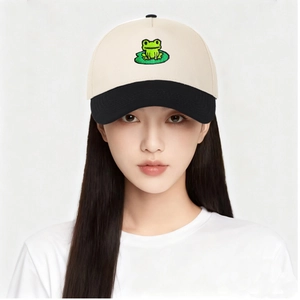 Detailed close-up of frog and lotus leaf embroidery on the cream and black baseball cap