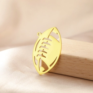 Detail of a gold stainless steel rugby pendant leaning on a light wooden block texture