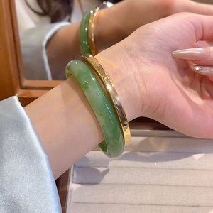 Detail showing stacked resin jade-green bangle and polished golden metal cuff on wrist