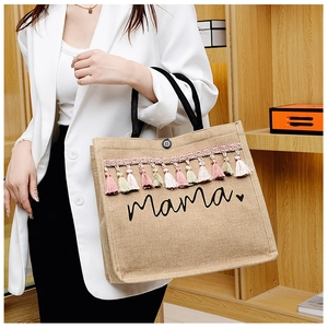 Close-up of linen jute tote bag with Mama print and colorful tassels on a wooden shelf