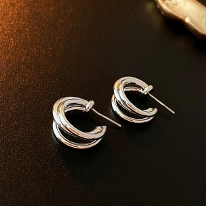 Macro shot of silver multi-layer C-shaped metal hoop earrings on dark leather background