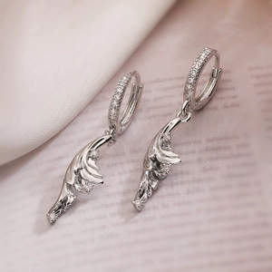 Elegant silver feather drop earrings with sparkling cubic zirconia on soft silk background