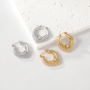 Close-up of heart-shaped pearl earrings with gold and silver zircon inlay on stone surface