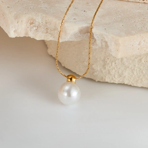 Detail of a large white pearl pendant on a gold snake chain over a beige stone