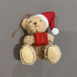 Detail of brown plush Christmas bear wearing a red hat and holding a festive gift box