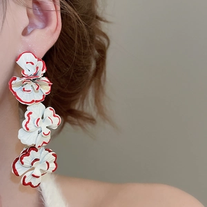 Detail of floral tassel earrings with white layered petals and red trimmed edges on model