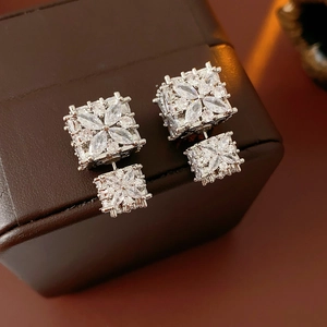 Détail de boucles d'oreilles carrées en zircon argenté sur une boîte en cuir brun