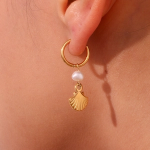 Macro shot of gold hoop earring with white pearl and golden seashell pendant detail
