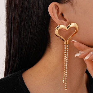 Close-up of a model wearing large gold heart earrings with dangling rhinestone tassels