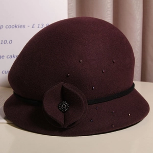 Dettaglio cappello cloche in feltro bordeaux con fiore 3D, nastro nero e perle colorate