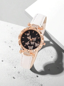 Close-up of rose gold watch with rhinestone butterflies on black dial and white leather strap