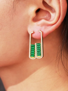 Macro shot of gold emerald zircon U-shaped earrings worn by a model in detail